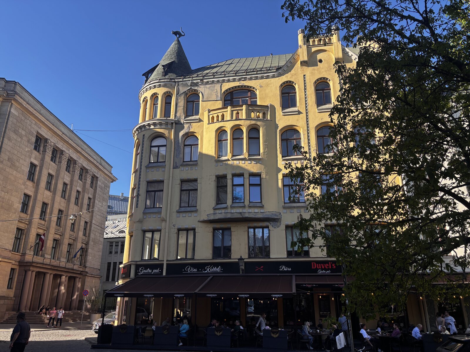 A Casa dos Gatos (Kaķu nams) na Meistaru iela, na Cidade Velha de Riga, com a sua fachada amarela Art Nouveau e o gato de bronze na torre de canto, Letónia.