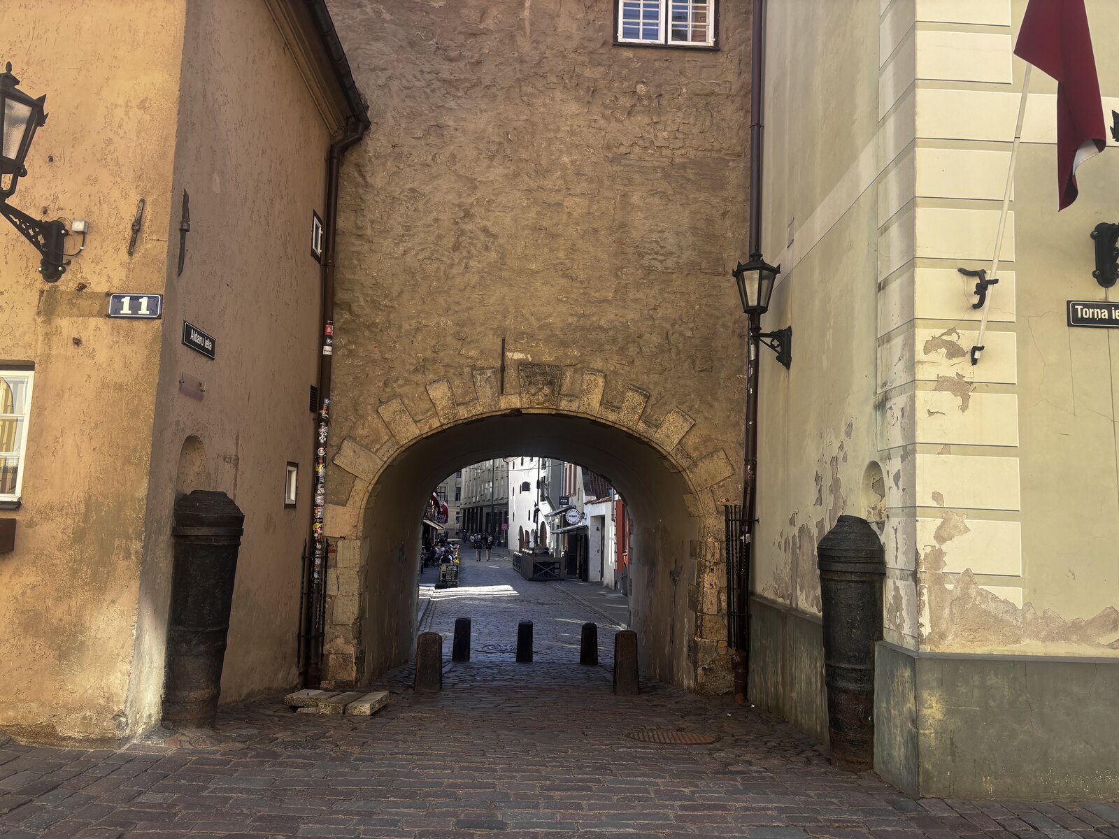 A Porta Sueca (Zviedru vārti) na Torņa iela, na Cidade Velha de Riga, Letónia, um arco de pedra entre dois edifícios amarelos.