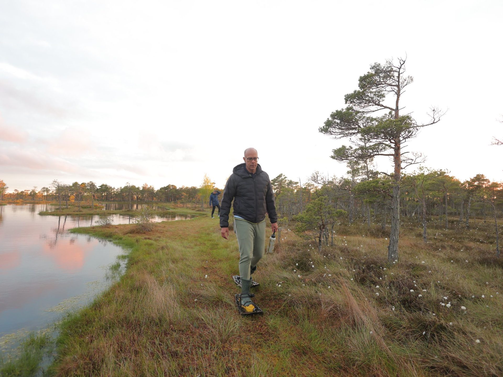 Caminhante solitário com as raquetes junto a uma poça que reflete a luz rosa do amanhecer