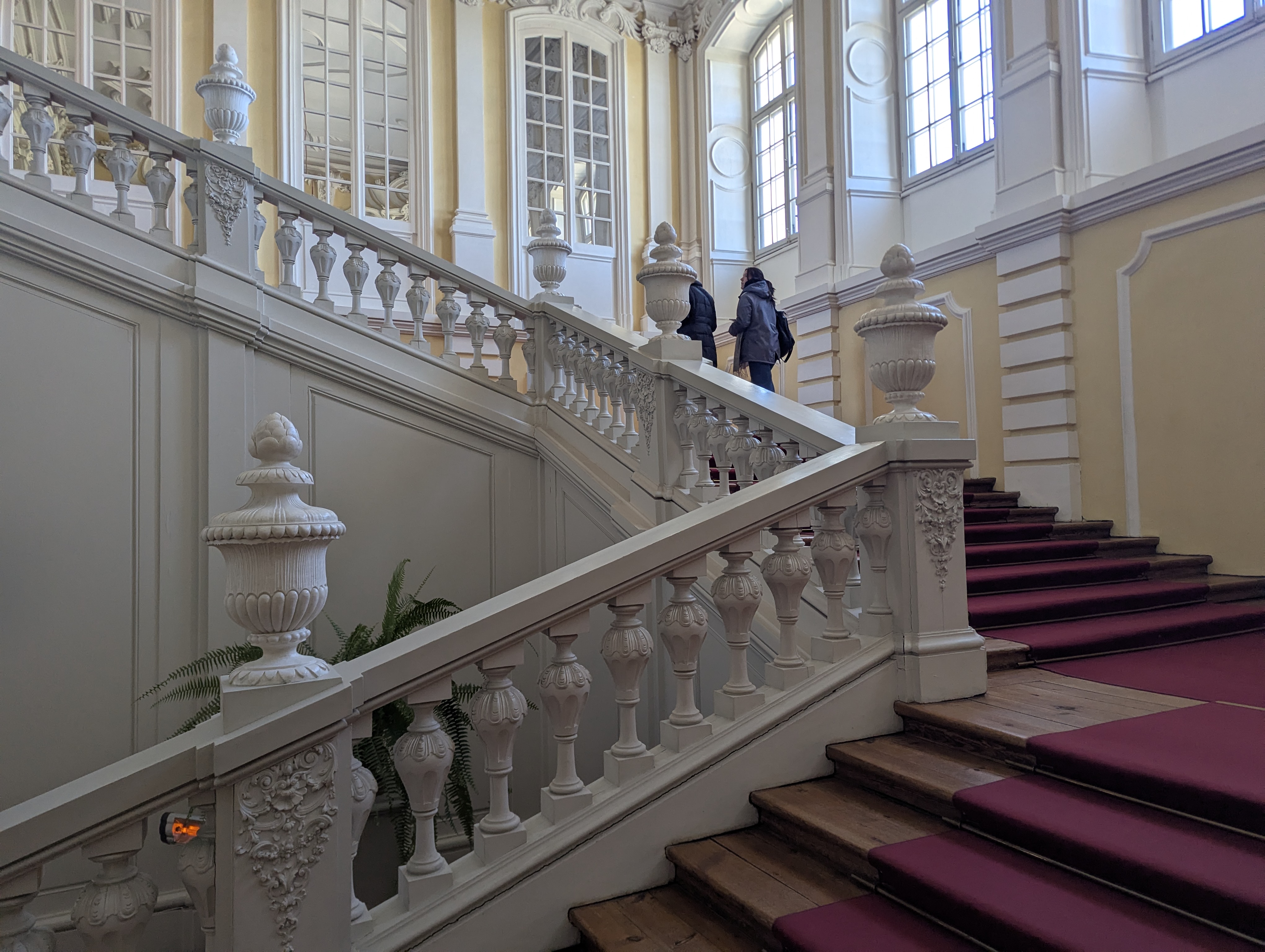 Escadaria de honra do Palácio de Rundāle com balaústres de estuque branco e tapete grená