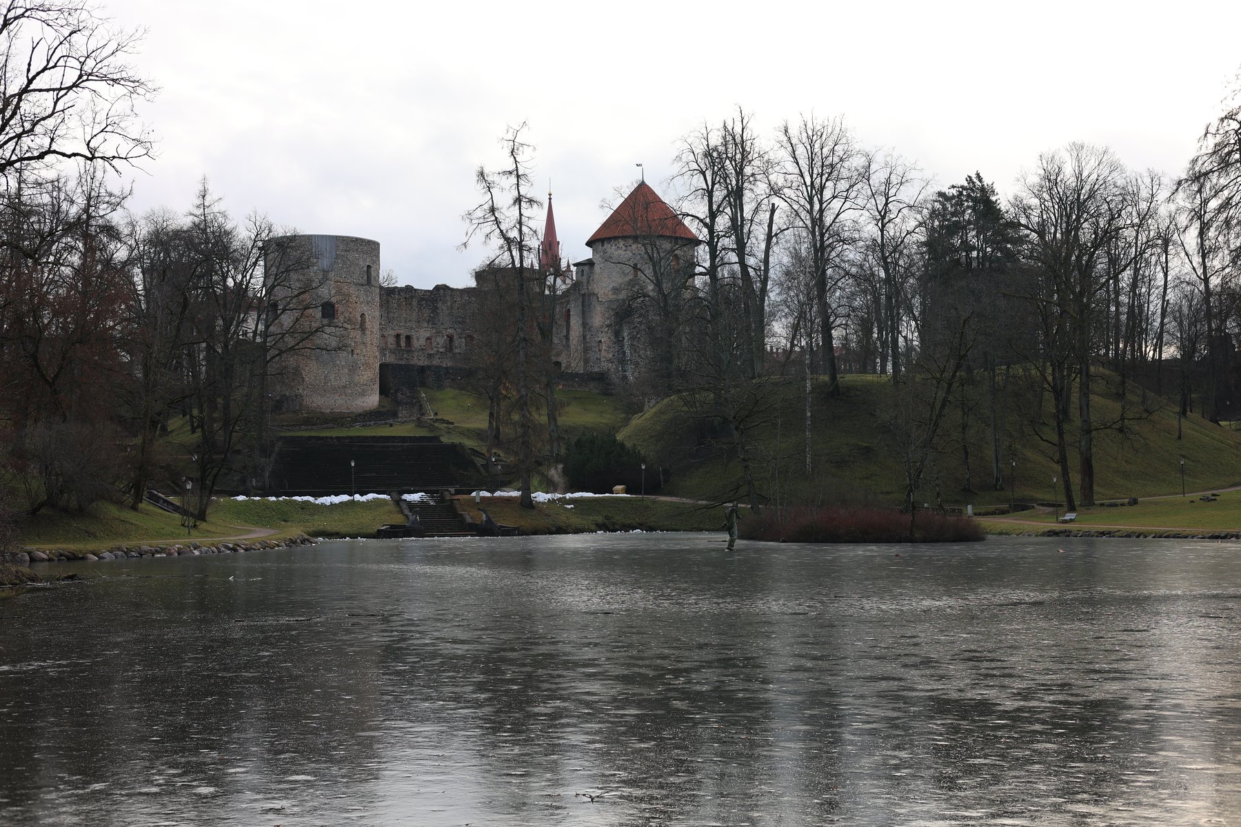 Castelo de Cēsis refletido num lago de inverno com árvores despidas