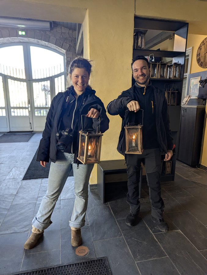 Dois hóspedes da Barefoot Baltic a sorrir com lanternas de vela acesas na mão, prontos para a visita ao castelo medieval à luz das velas