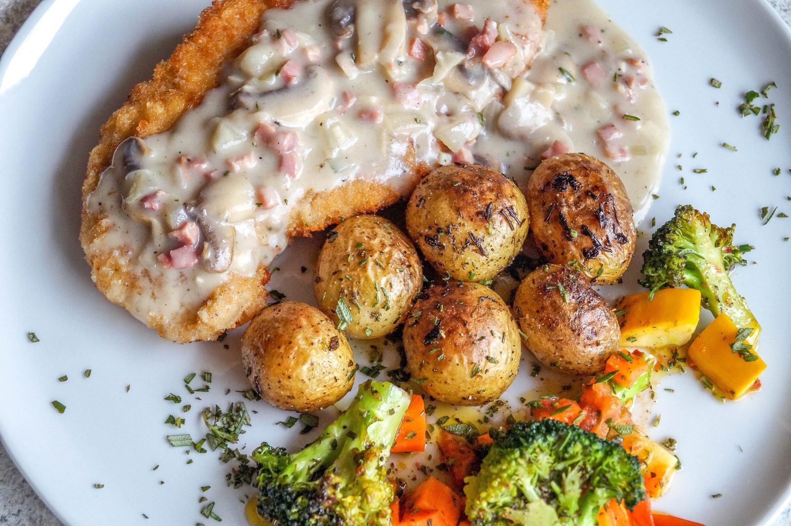 Um prato de karbonāde, costeleta de porco panada letã, com molho cremoso de cogumelos, batatas com ervas e legumes assados