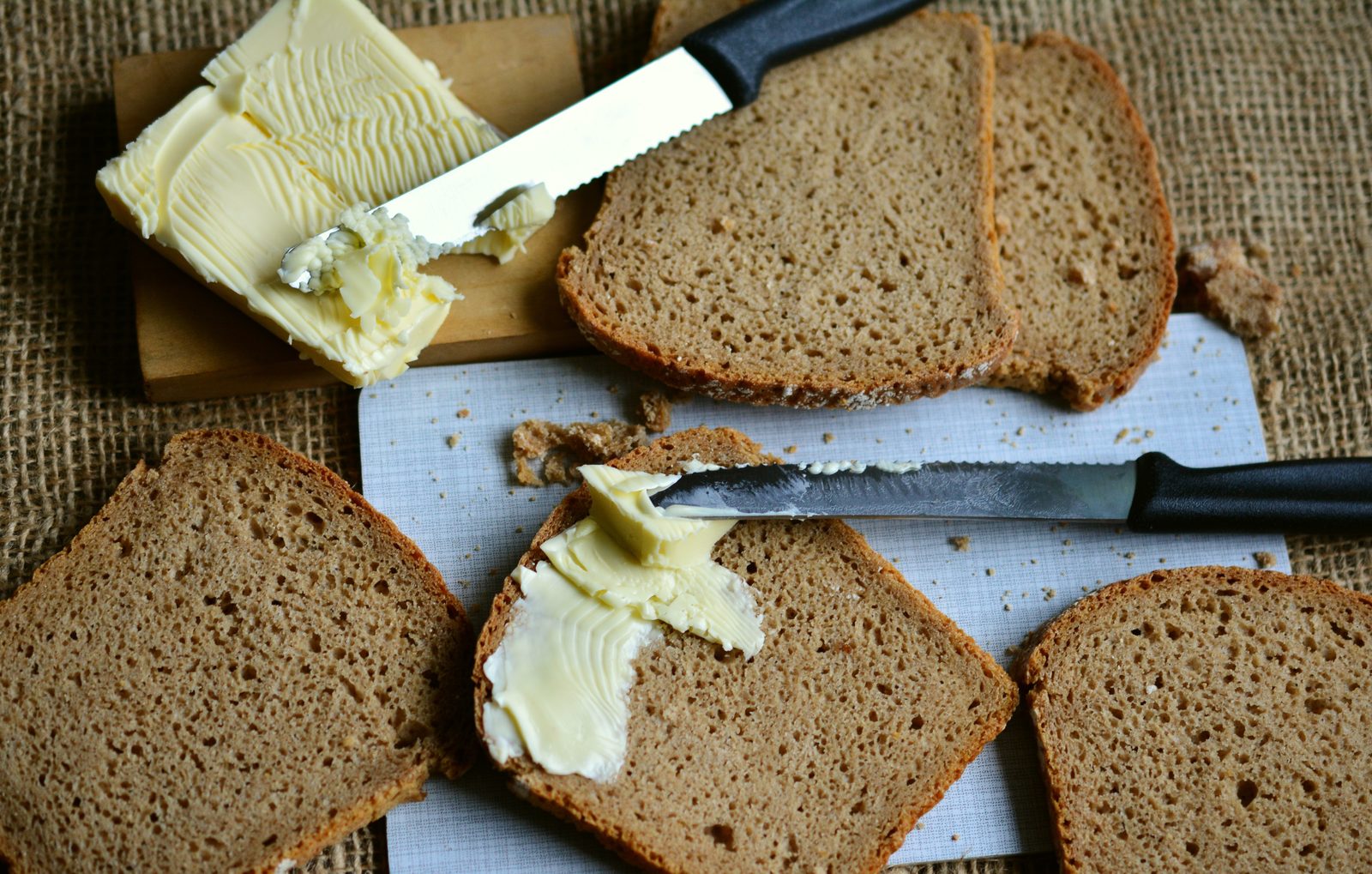Fatias de pão de centeio letão rupjmaize com manteiga e uma faca sobre serapilheira